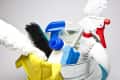 Cleaning supplies in a metal bucket, including brushes, spray bottles, a sponge, and yellow rubber gloves.