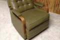 Olive green vintage recliner with wooden armrests against wood-paneled wall.
