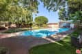 Backyard with a rectangular swimming pool, surrounded by trees, brick patio, and lounge chairs.