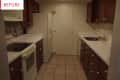 Narrow kitchen with dark wood cabinets, white countertops, and appliances, including a fridge and stove.