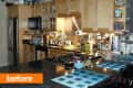 Cluttered kitchen with wooden cabinets, stainless steel appliances, and mosaic tile backsplash.