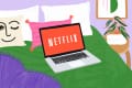 Laptop displaying Netflix on a bed with colorful pillows, a plant, and wall art in a cozy room.