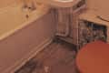 Outdated bathroom with pink tile, white sink, bathtub, and wooden floor.