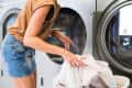 Person loading white laundry into a front-loading washing machine at a laundromat.