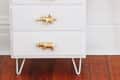 White desk with gold animal drawer handles, pink lamp, wire organizer, and pencil on top.