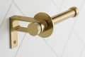 Gold toilet paper holder mounted on white tiled wall.