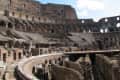 Interior view of the Colosseum in Rome, showcasing ancient stone arches and tiered seating under a clear sky.