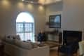 Spacious living room with vaulted ceiling, beige sectional sofa, polka dot chairs, and large arched window.