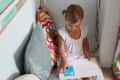 Child reading a book in a cozy nook with colorful pillows and wall shelves filled with books.