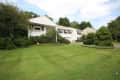 White two-story house with black shutters, surrounded by lush greenery and a well-maintained lawn.