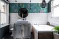 Bathroom with a rustic vanity, round mirror, white tiles, floral wallpaper, and a bathtub with plants and toiletries.