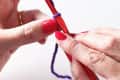 Hands holding a red crochet hook with purple yarn, demonstrating a crochet technique.