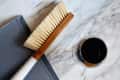 Wooden-handled brush on a marble surface next to a glass of dark liquid and a gray mat.
