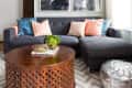 Gray sectional sofa with colorful pillows, wooden coffee table, silver pouf, and abstract black-and-white wall art.