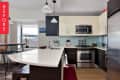 Modern kitchen with white island, stainless steel appliances, dark cabinets, and pendant lights.