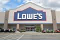 Lowe's storefront with garden equipment, plants, and lawn mowers displayed outside.
