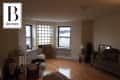 Living room with hardwood floors, gray sofa, boxes, bar cart, and large windows.