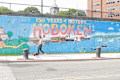 Mural celebrating 150 years of Hoboken history with boats and cityscape, woman walking dog in foreground.