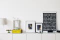 White sideboard with framed art, a London sign, a lamp, and decor items including a yellow box and green glass stand.