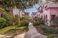 Mediterranean-style courtyard with pink stucco buildings, lush greenery, and a winding stone path.