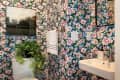 Bathroom with floral wallpaper, white sink, towel, and a potted plant on the toilet tank.