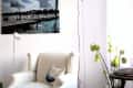 Cozy reading nook with a white armchair, floor lamp, and wall art of a pier. Green floral decor adds a fresh touch.