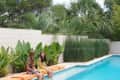 Two women sitting on orange cushions by a pool, surrounded by lush greenery and palm trees.
