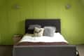 Gray bed with white and brown bedding, decorative pillows, and green paneled walls in a cozy bedroom.