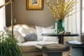 Cozy living room with beige sofa, patterned pillows, brass lamp, and a vase of yellow flowers on a round table.