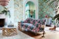 Living room with pink floral sofa, rattan coffee table, and pastel wallpaper, featuring a dog on a rug near a decorative bust.