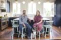 Couple sitting on mint green chairs in a modern kitchen with dogs, navy cabinets, and pendant lights.