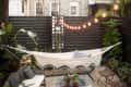 Cozy backyard with a hammock, string lights, bench, glass table, and potted plants on gravel.