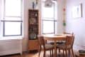 Mid-century dining room with round wooden table, four chairs, tall shelf, and arc floor lamp by two large windows.