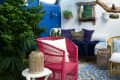 Colorful patio with pink chair, blue and white tiles, wicker furniture, and lush greenery against a blue wall.