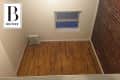 Small empty room with wooden floor, exposed brick wall, radiator, and a single window.