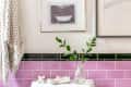 Bathroom with pink subway tiles, framed art, a towel, and a vase with green leaves on the toilet tank.