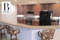 Kitchen with brown cabinets, black appliances, beige countertops, and wicker bar stools.