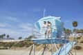 Two people standing on a blue lifeguard tower overlooking a sandy beach with palm trees.