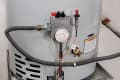 Gas water heater with temperature control dial, warning label, and connected pipes.