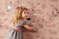 Child in a gray dress playing with animal magnets on a pink patterned wallpaper.