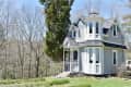 Victorian-style tiny house with turret, white siding, and surrounded by trees.