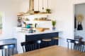 Modern kitchen with white cabinets, open shelves, a blue pot on the stove, and wooden stools at the island.