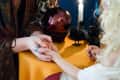 Fortune teller reading a woman's palm at a table with a candle, crystal ball, and decorative crows.