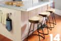 Kitchen with gray walls, marble island, wooden stools, pendant light, and a vase with flowers.