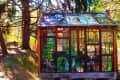 Stained glass greenhouse in a forest setting with colorful plant and mushroom designs on the panels.