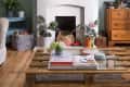 Living room with a white fireplace, round mirror, bookshelves, plants, and a wooden coffee table with magazines.