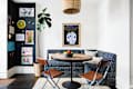 Cozy dining nook with round wooden table, blue patterned banquette, two brown chairs, and colorful wall art.