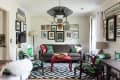 Eclectic living room with a brown sofa, red coffee table, patterned chairs, and a gallery wall of framed photos.