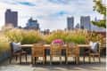 Rooftop patio with wooden dining set, pink flowers, and city skyline view.