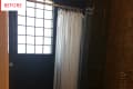 Shower area with white curtain, glass block window, and dark tiled walls.